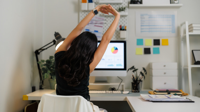 woman stretching in home office with pegboard wall and desk organizers