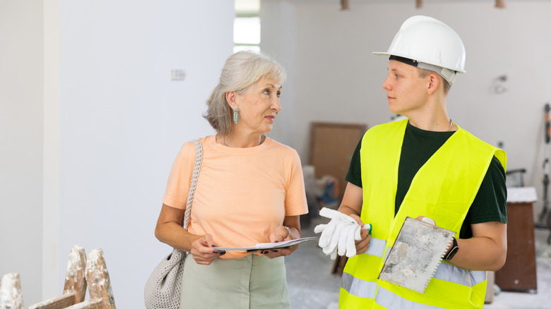 A woman with papers talking to a construction worker.