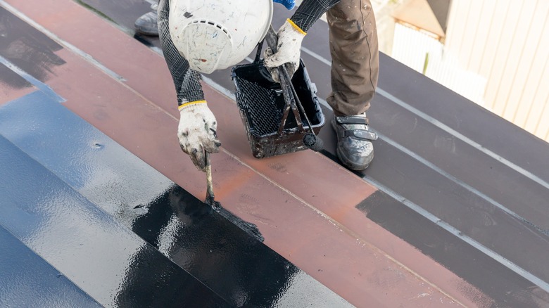 A male worker painting a metal roof in black