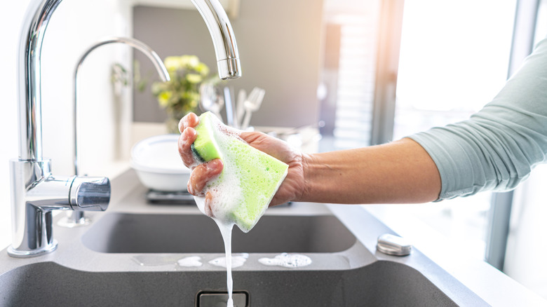 Hand washing a soapy dishwashing sponge in sink