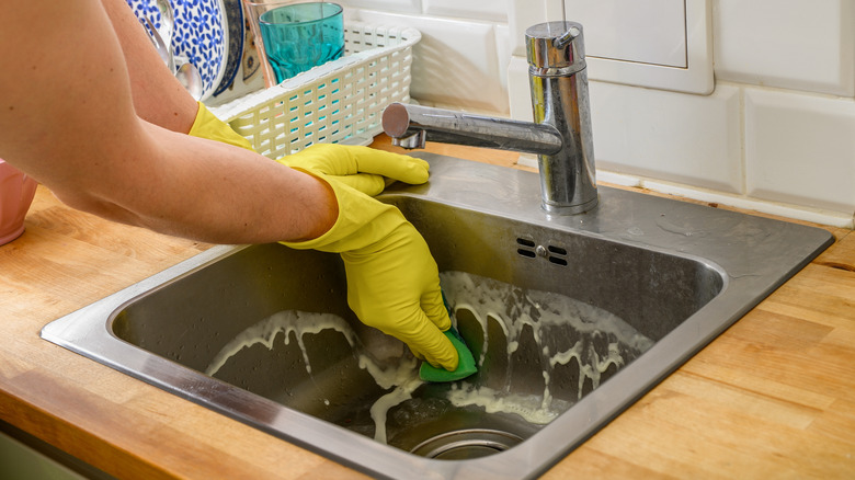 Gloved hands scrubbing a stainless sink in kitchen
