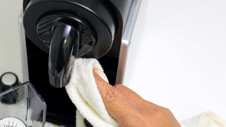 Hand wiping a coffee machine's exterior with white cloth