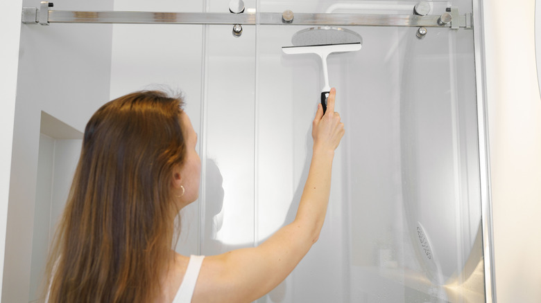 Woman running a squeegee over a glass shower door