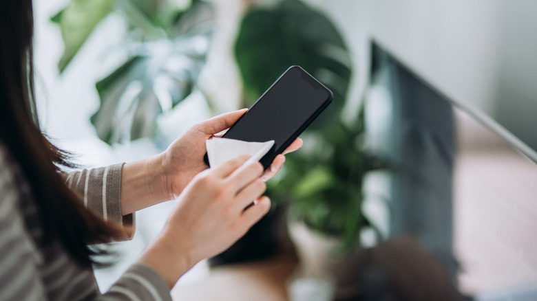 Hands wiping the glass screen of a smartphone