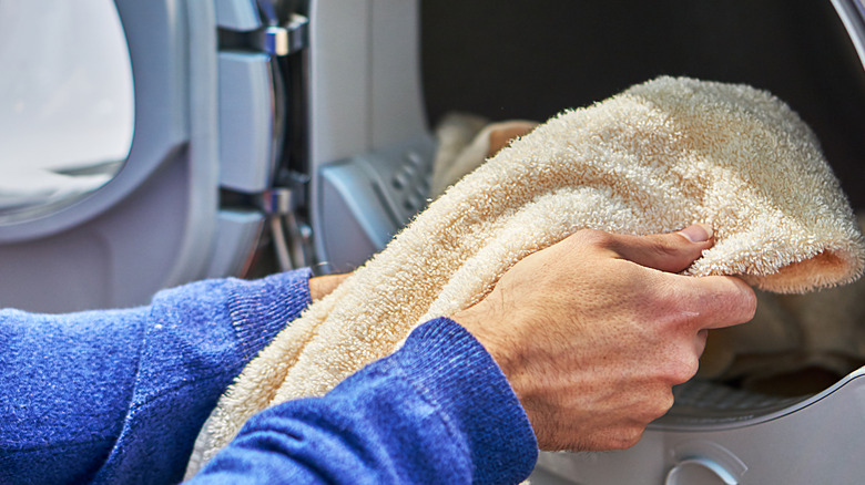 Hand putting in yellow towel in washing machine
