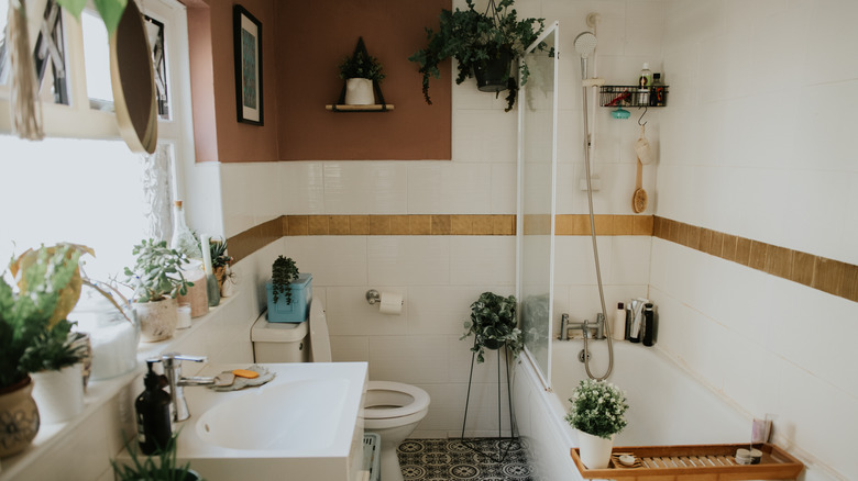 A white bathroom filled with plants that sit on the sink and hang from the ceiling.
