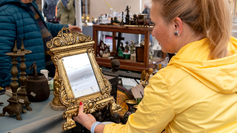 A woman looks at an ornate gold mirror in an antique shop.