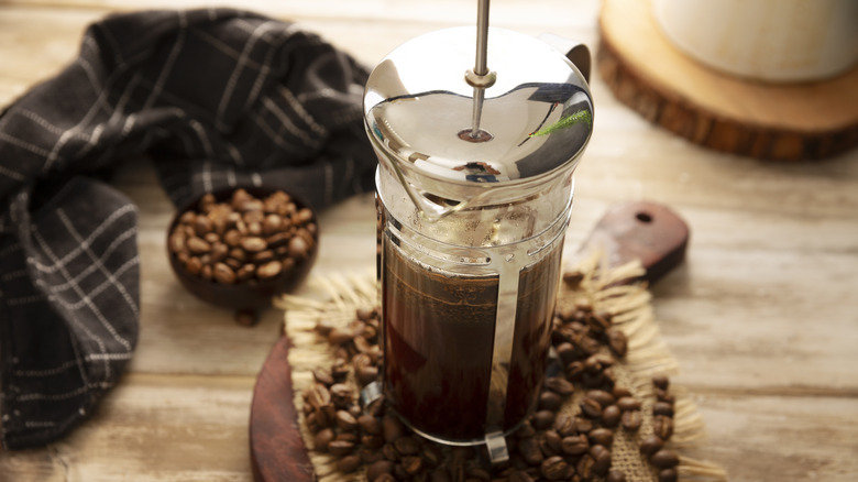 A French press coffee pot sitting on a bed of coffee beans