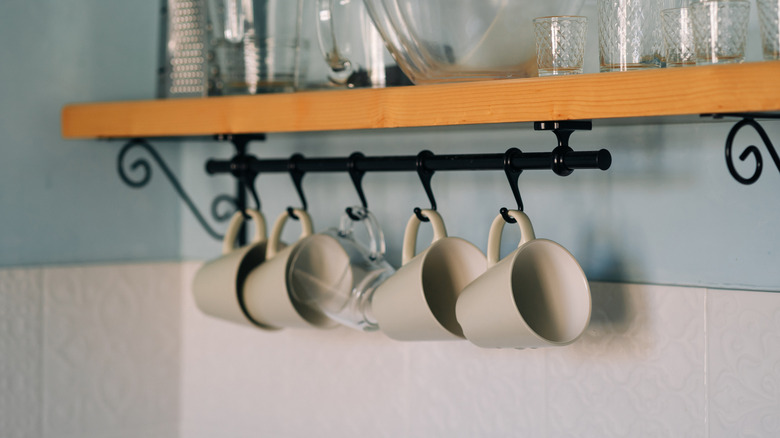 Mugs hung on bar with hooks under a floating shelf