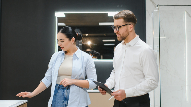 Woman looking at bathroom features and man with clipboard helping to plan design.