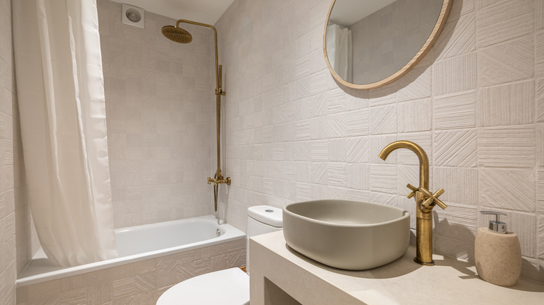 Neutral beige bathroom with textured wall tiles, brass fixtures, and stone countertop.