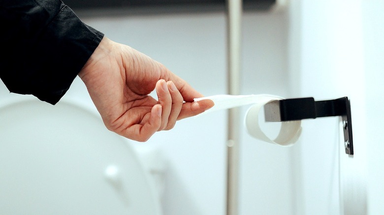 A hand tears off the final squares from a roll of toilet paper