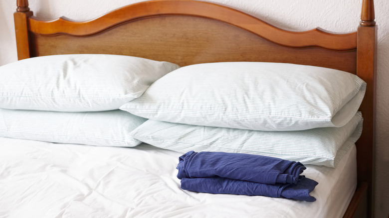 A bed with four flat pillows on top, a white sheet, and a folded blue sheet