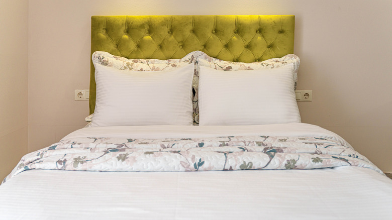 A bed made with white sheets, and a light loral pattern on the duvet and two pillows, and a lime green velvet headboard
