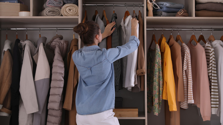 A woman standing in front of her closet, looking at shirts