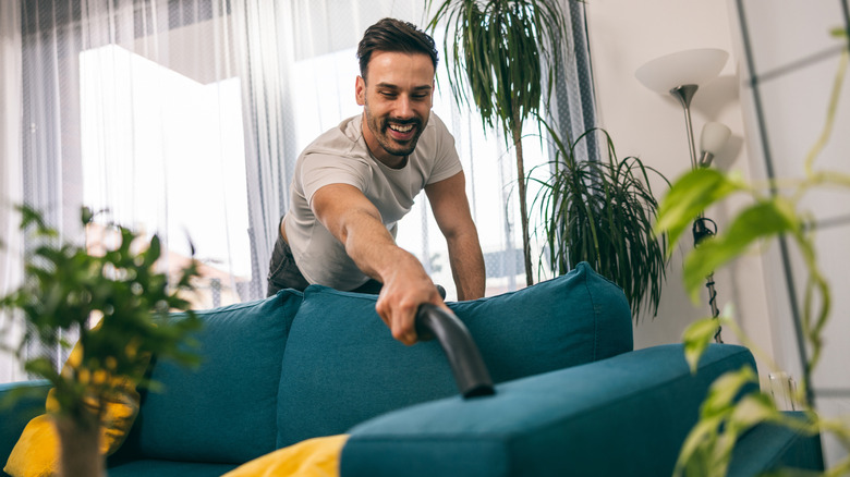 Man vacuuming a blue couch