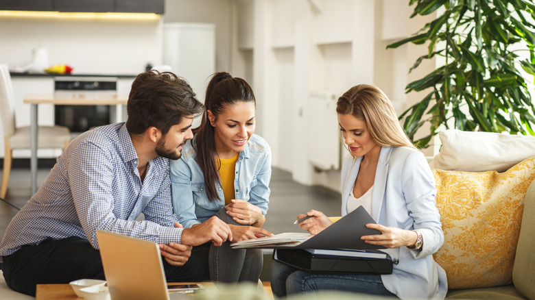 Smiling couple looking at documents a female is showing them