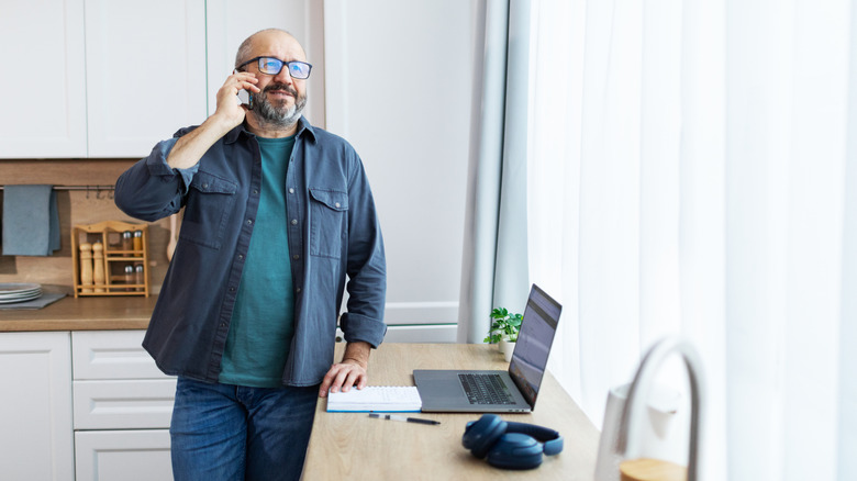 Man speaking on phone and has a laptop and notebook in front of him