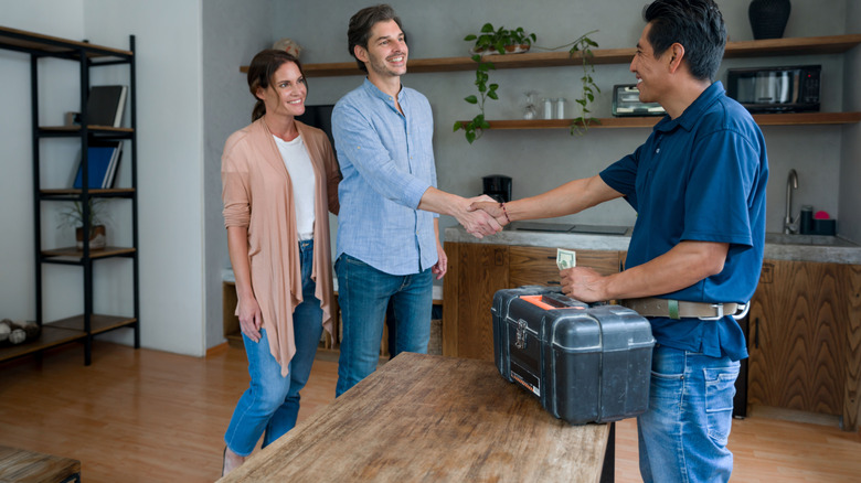 A happy couple shaking hands with a plumber