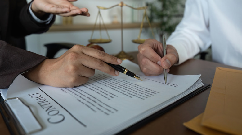 Hand pointing with a pen while a man signs a contract