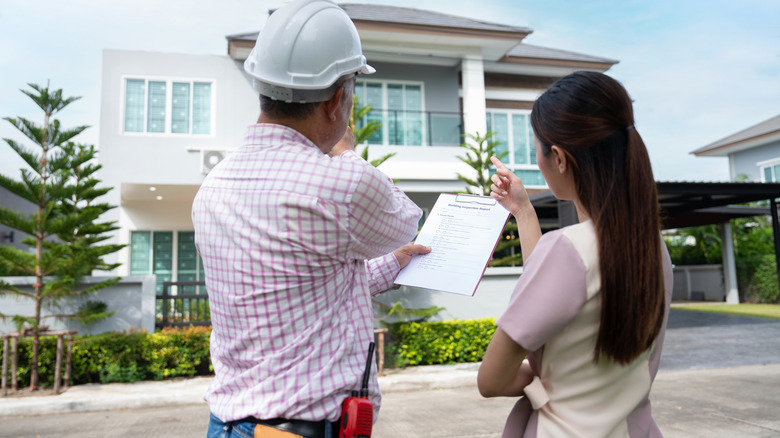 Woman speaking with a man in a hard hat in front of a home