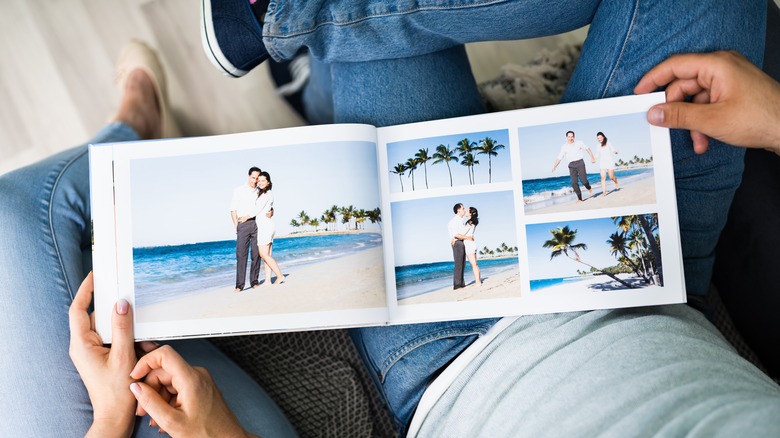 The hands of a couple looking through a vacation photo album in their laps.