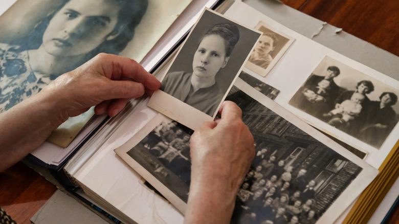 Hand holding a vintage black and white photo of a woman in front of an album of similar photos.