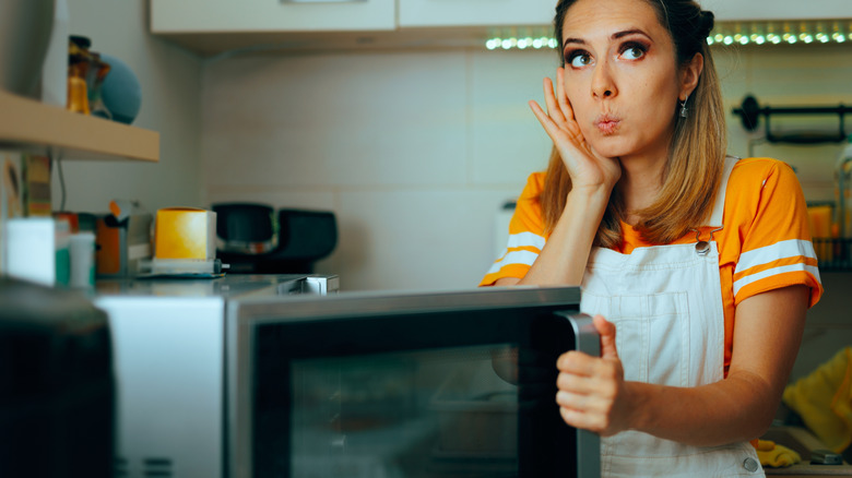 Woman holding the door of a microwave with a finger pressed to her ear