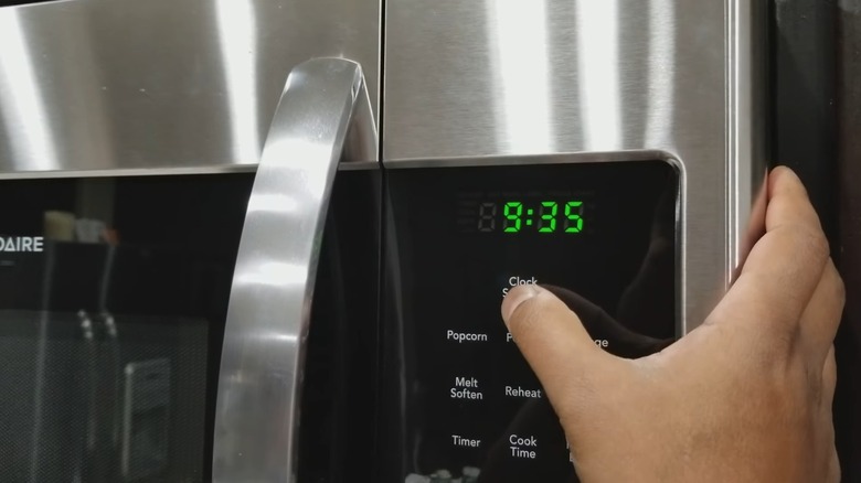 A male is pressing the Clock Settings button on a microwave