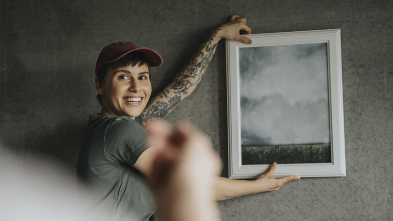 Person holding up framed picture to wall