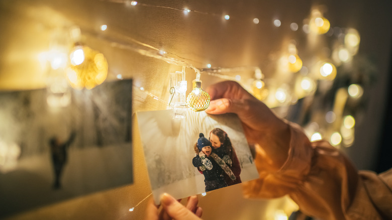 A hand hanging up photos with small string lights around it