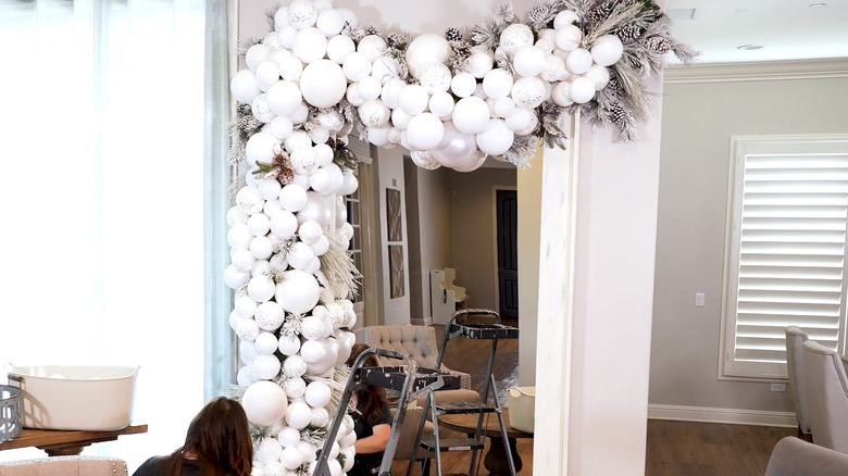 A garland around a mirror with large white baubles and frosted greenery and pinecones
