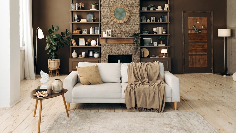 A living room with brown walls, bookcases and a sofa with small table beside it.