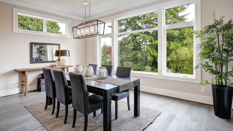 A dining room with black table and chairs against big picture windows.