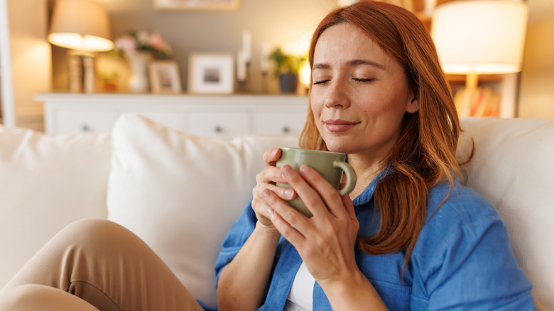 A person sitting on the lounge with a cup of coffee and a happy and relaxed look on her face