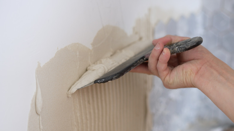 Hand applying adhesive to a wall using trowel for tile installation