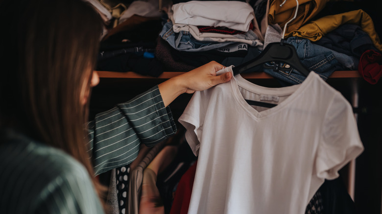 Woman holding white t-shirt on hanger in a dimly lit closet