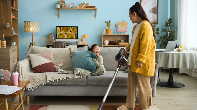 person vacuuming living room while kid sits on couch
