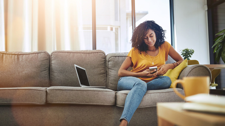 young woman using cell phone relaxing on couch in living room
