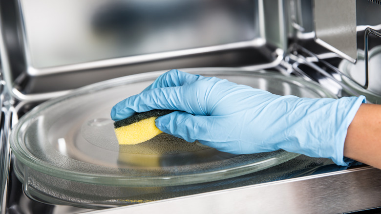 Gloved hand cleaning inside microwave