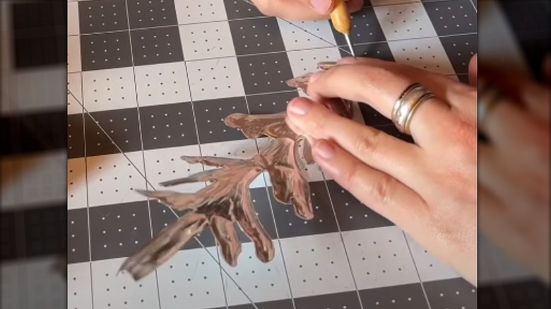 A pair of hands emboss a tree shape cut from a beer can.