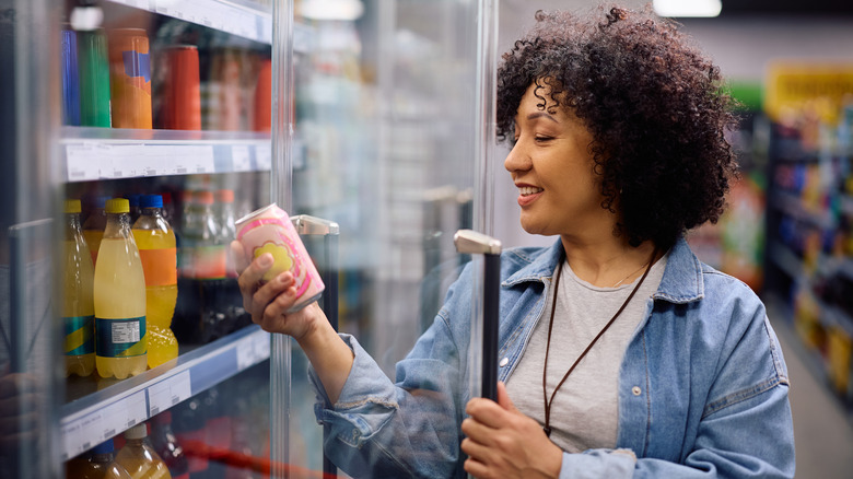 A happy woman chooses a can of soda at a grocery store.