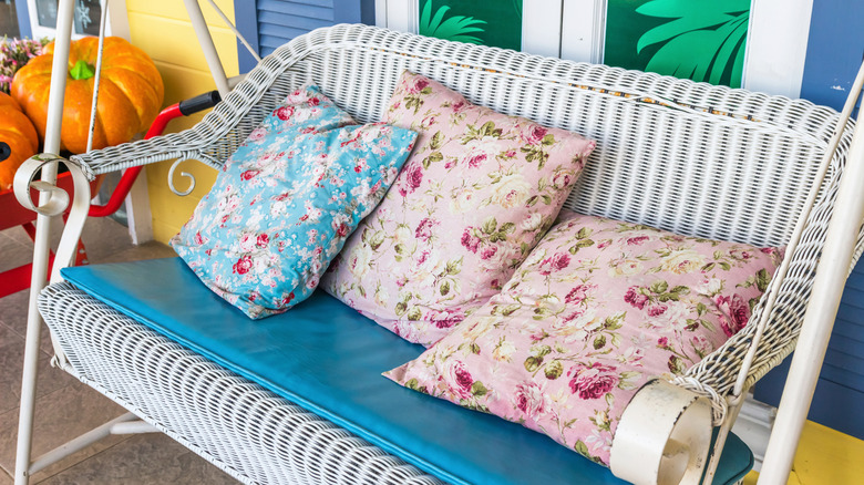 Colorful, floral, vintage-looking outdoor pillows on a white wicker swing.