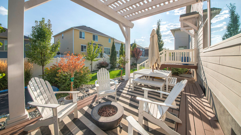 back of a home white pergola containing white outdoor furniture, brazier, and umbrella