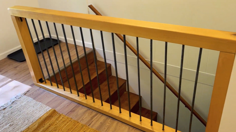 A DIY rebar and lumber railing at the top of a set of stairs in a two-floor home.