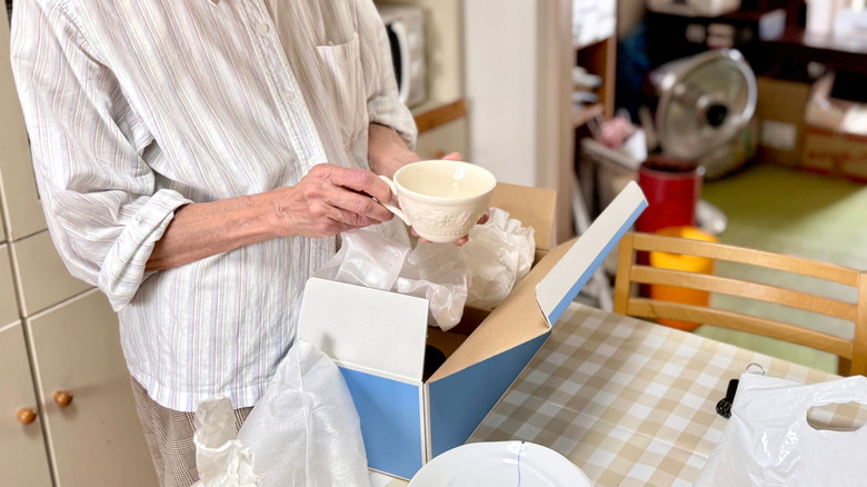 An elderly person holds a vintage ceramic teacup while decluttering.