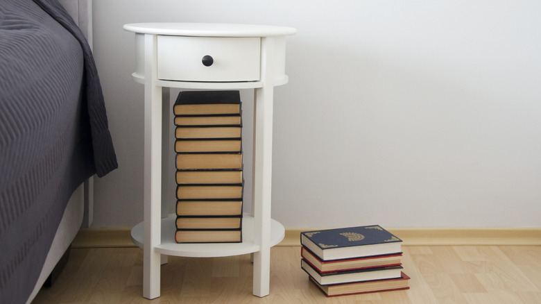 A white nightstand with an open bottom shelf stacked with books.