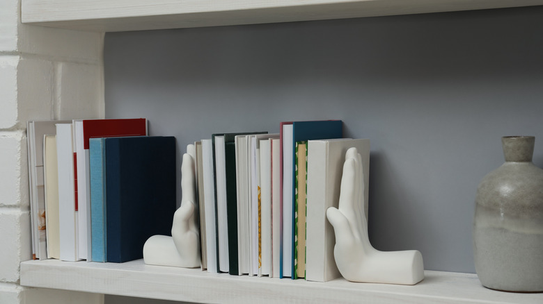A shelf with two separate groups of books, one held together with hand-shaped bookends.