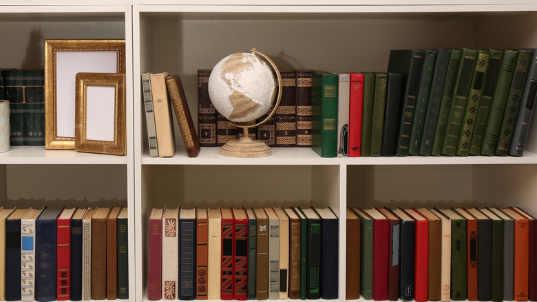 Close-up of a bookcase with shelves of hardcover books, gold picture frames, and a globe.