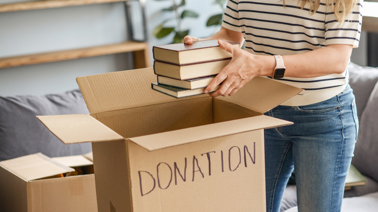 Person lowering a stack of books into a cardboard box labeled donation.